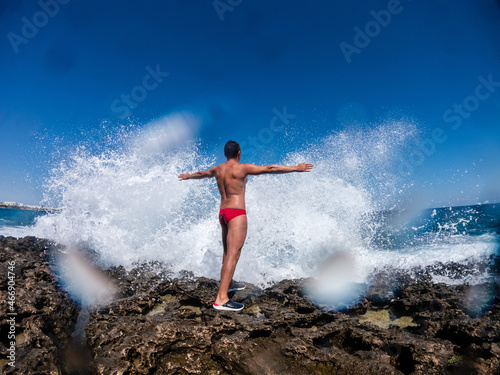 Man standing on cliff during storm in sea. Splashes of ocean waves