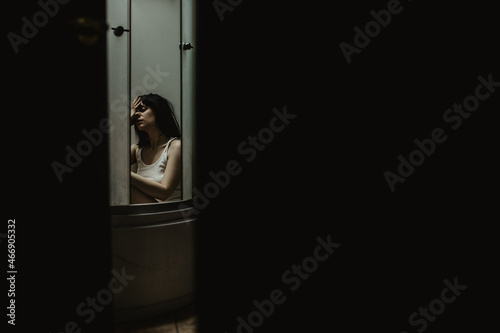 The girl is sitting in the shower, in the bathroom. She is upset, she is depressed. The door is ajar