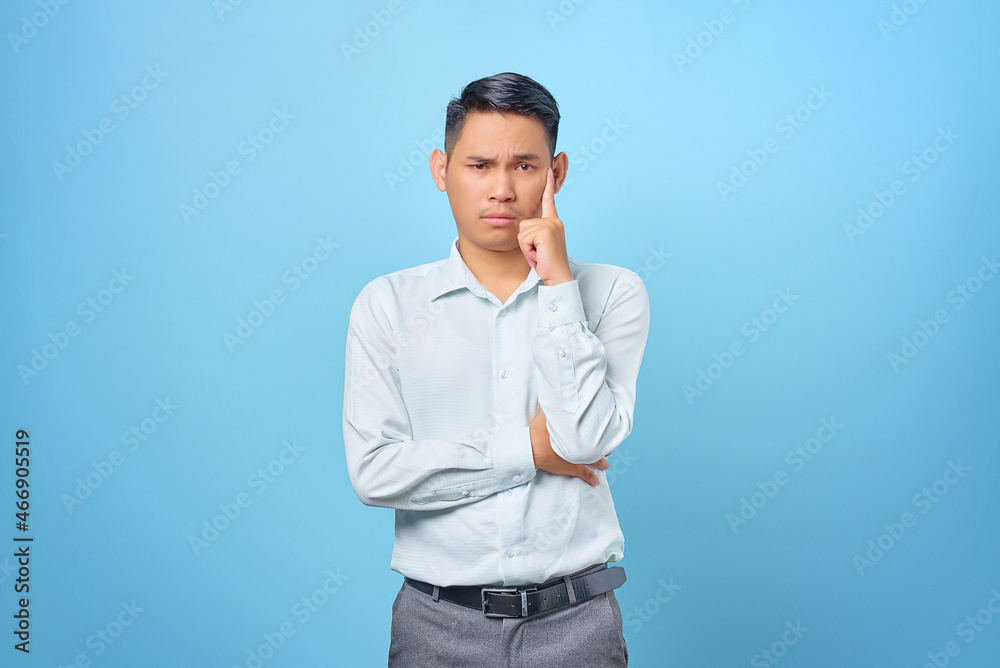 Pensive young handsome businessman thinking about questions on blue background