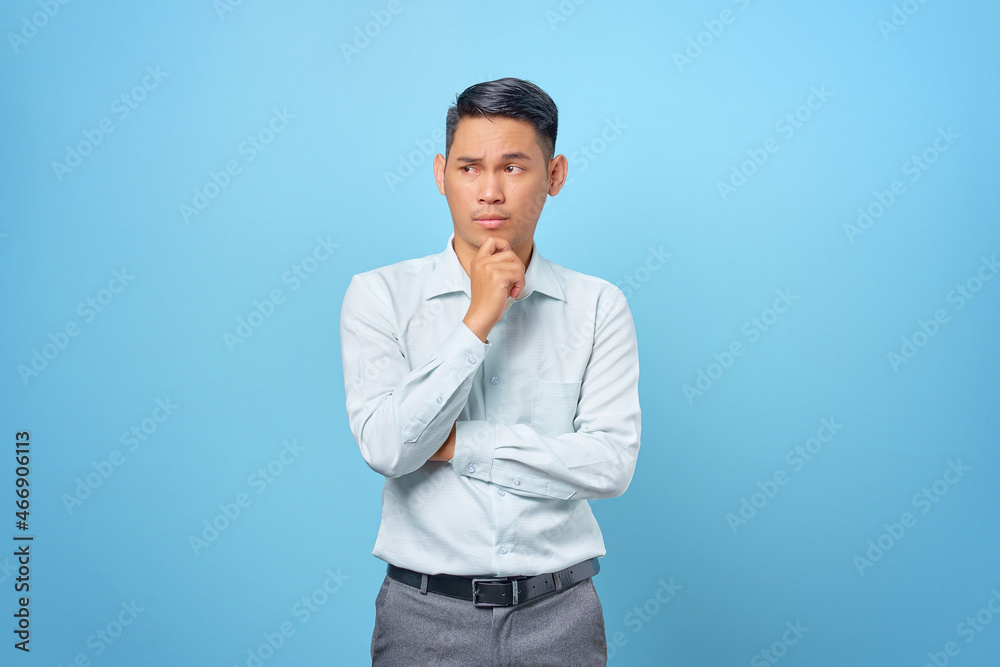 Pensive young handsome businessman rubs chin and thinking about a question on blue background Pensive young handsome businessman rubs chin and thinking about a question on blue background
