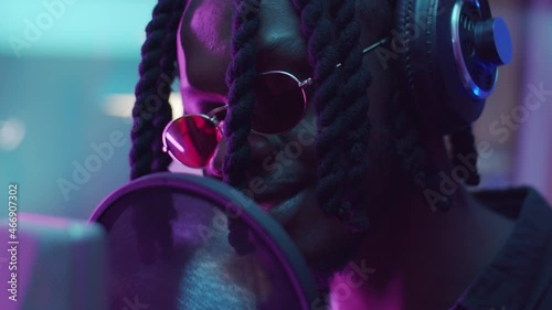 Close up shot of African American man with dreadlocks singing in mic and then taking off sunglasses while recording rap song in audio production studio photo