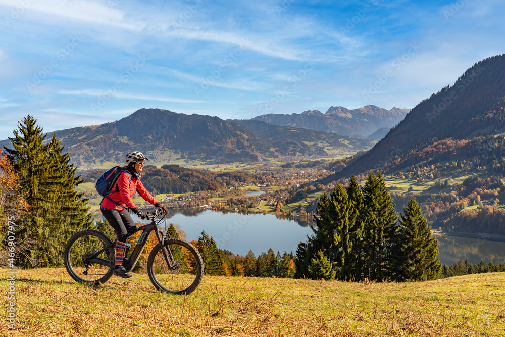 nice  woman with electric mountain bike enjoying the view over lake  Alpsee in atumnal atmosphere  in the Allgaeu alps above  Immenstadt, Bavarian Alps, 
