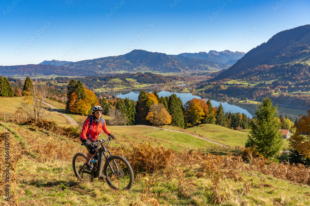 nice woman with electric mountain bike enjoying the view over lake Alpsee in atumnal atmosphere in the Allgaeu alps above Immenstadt, Bavarian Alps, nice woman with electric mountain bike enjoying the view over lake Alpsee in atumnal atmosphere in the Allgaeu alps above Immenstadt, Bavarian Alps,