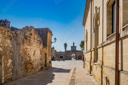 Fototapeta Naklejka Na Ścianę i Meble -  The small fortified village of Acaya, Lecce, Salento, Puglia, Italy. The stone-paved square. An alley of the village leads to the large entrance door, with the large arch and the stone statue.