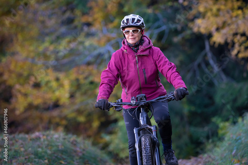 ympathetic active senior woman, riding her electric mountainbike in the colorful autumn forests of the Bavarian Alps near Oberstaufen, Germany