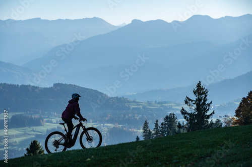 Woman as silhouette riding her electric mountain bike in the Allgaeu alps near Oberstaufen with awesome view into the Bregenz Wald Mountains, Vorarlberg , Austria, people 
