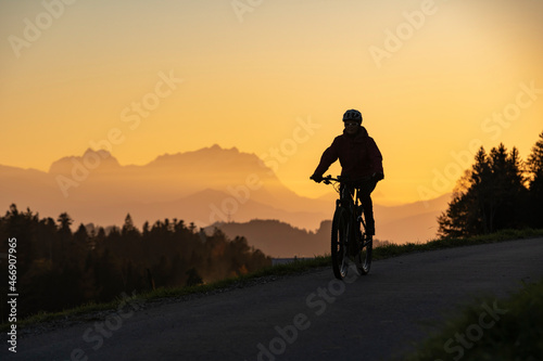 active woman riding her electric mountain bike at sunset in front of the awesome silhouette of Mount Saentis  Appenzell switzerland