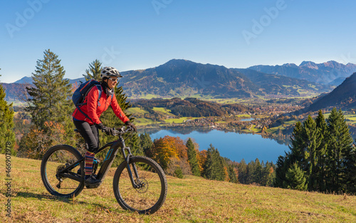 nice woman with electric mountain bike enjoying the view over lake Alpsee in atumnal atmosphere in the Allgaeu alps above Immenstadt, Bavarian Alps, Germany