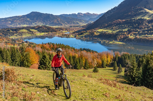 nice woman with electric mountain bike enjoying the view over lake Alpsee in atumnal atmosphere in the Allgaeu alps above Immenstadt, Bavarian Alps, 