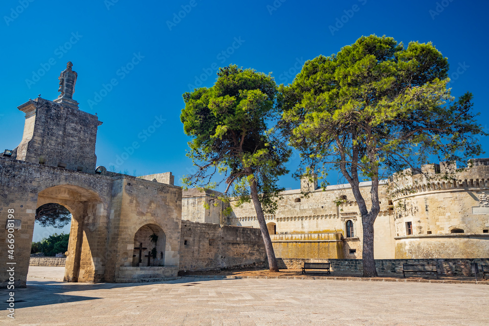 The small fortified village of Acaya, Lecce, Salento, Puglia, Italy. The large stone-paved square. The castle with the towers and the entrance door, with the large arch and the stone statue.