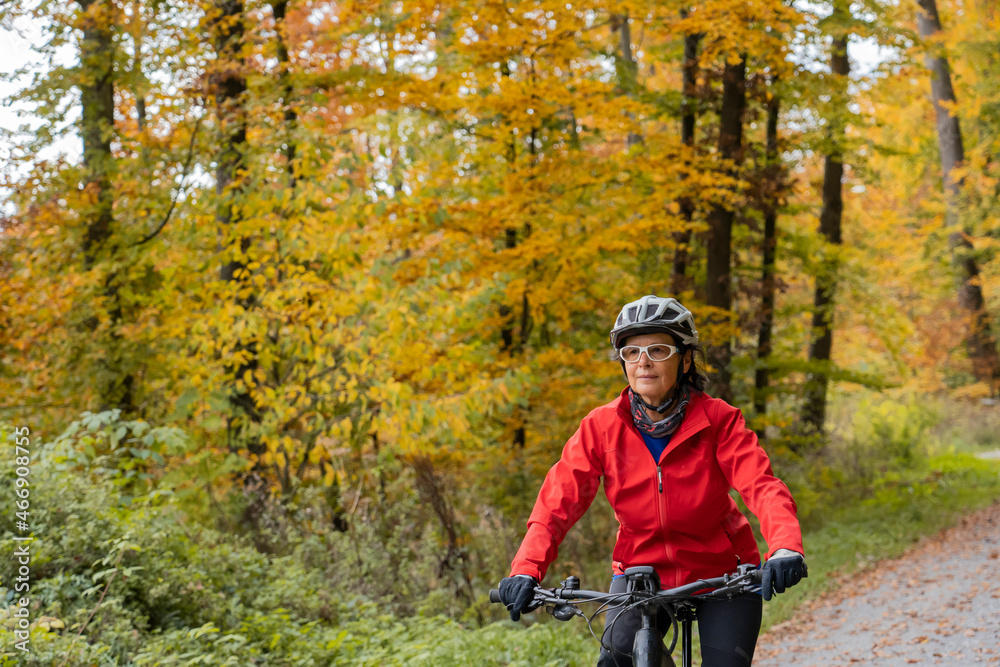 Obraz premium pretty senior woman ridin her electric bicycle in a colorful autumn forest with golden foliage 