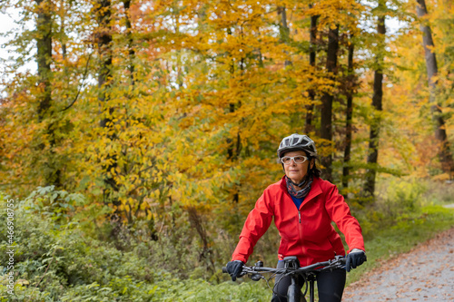 pretty senior woman ridin her electric bicycle in a colorful autumn forest with golden foliage
 photo