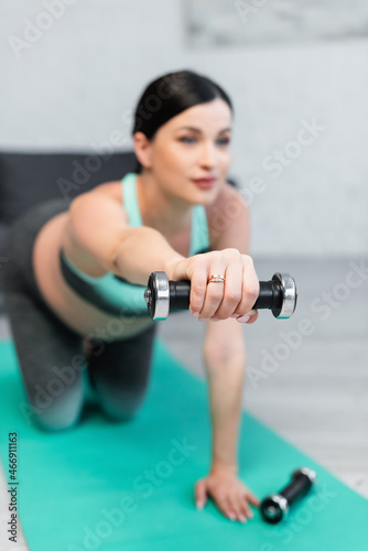 selective focus of dumbbell in hand of blurred pregnant woman training on fitness mat