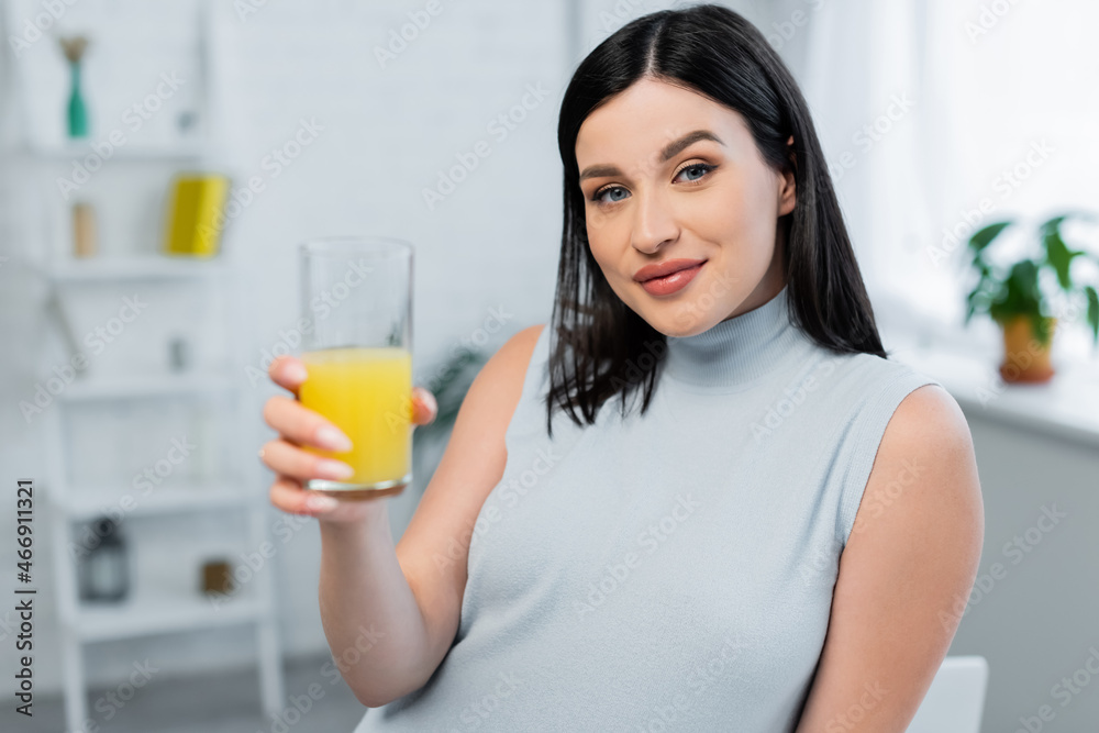 young woman looking at camera while holding glass of fresh orange juice young woman looking at camera while holding glass of fresh orange juice