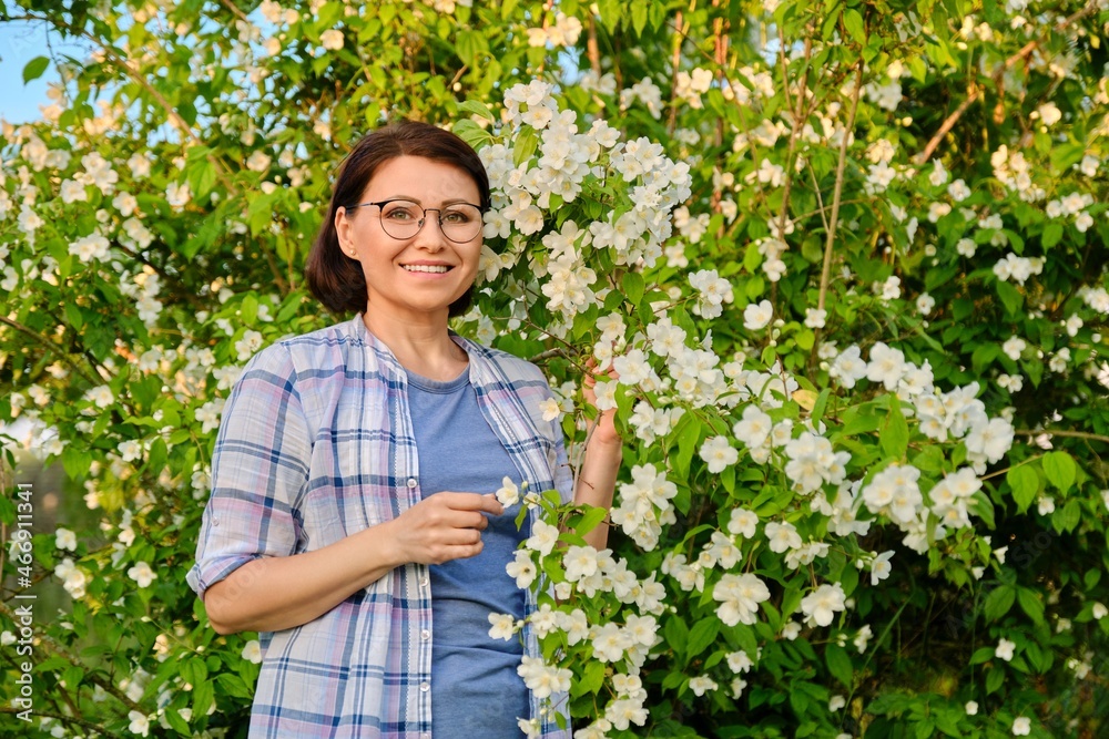 Portrait of a smiling middle-aged woman near a flowering jasmine bush. Portrait of a smiling middle-aged woman near a flowering jasmine bush.