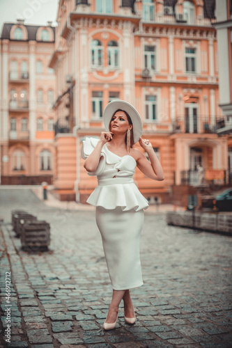 Close up fashionable woman portrait of young pretty fashionable girl posing in city in Europe, summer street fashion, holding retro hat. Fashion chic 