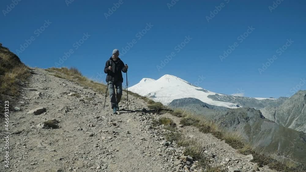 Slow motion - Hiker woman walking the edge of the canyon with Elbrus mountain background. People Hiking Mountains. Caucasus Mountains, Russia. Active Lifestyle Adventure Concept Slow motion - Hiker woman walking the edge of the canyon with Elbrus mountain background. People Hiking Mountains. Caucasus Mountains, Russia. Active Lifestyle Adventure Concept
