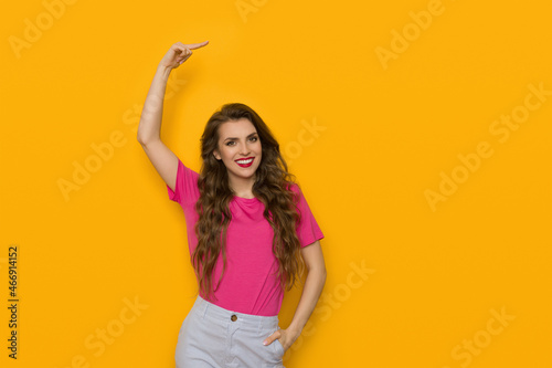 Smiling young woman is pointing above the head.