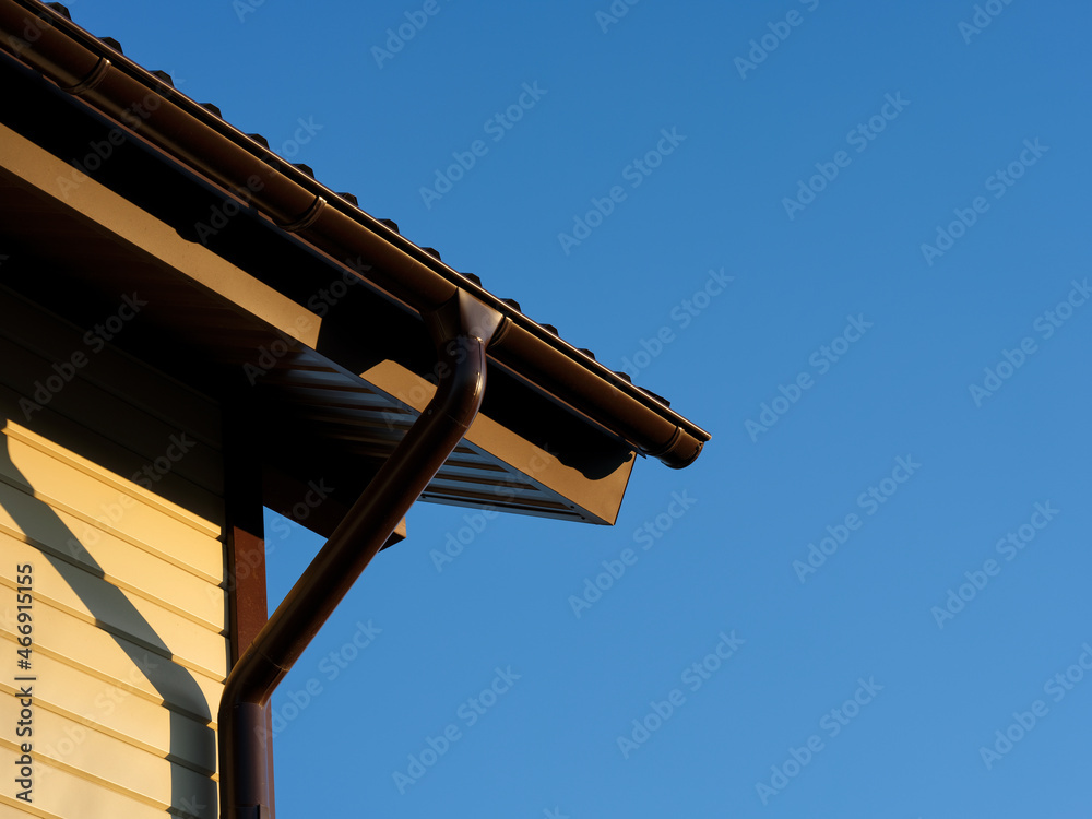 A roof with a gutter on a house against a blue sky background. A roof with a gutter on a house against a blue sky background.