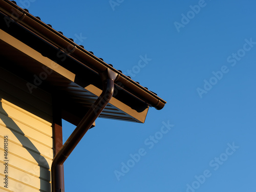 A roof with a gutter on a house against a blue sky background.