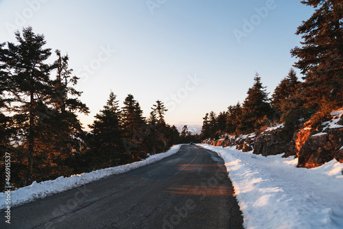 Empty winter asphalt road at sunset in the middle of mountainous area and coniferous snow-covered forest. Highlands of Greece, winter time. Freedom, travel concept photo