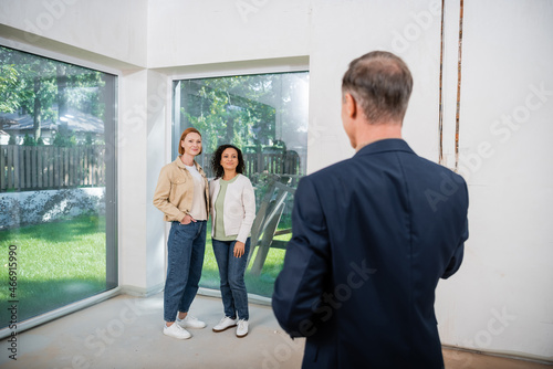 interracial lesbian couple looking at blurred realtor in modern house