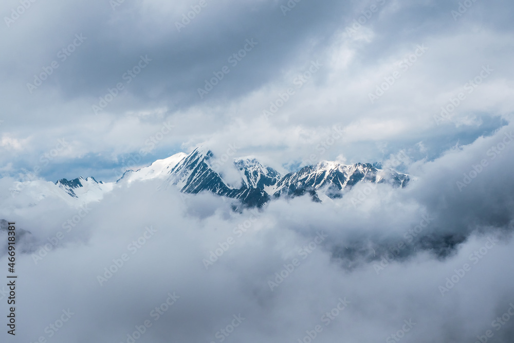 Wonderful minimalist landscape with big snowy mountain peaks above low clouds. Atmospheric minimalism with large snow mountain tops, dark glacier in dramatic sky.