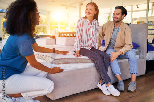 African American saleswoman helps customers choose an orthopedic mattress in a store. A young couple is buying a mattress and bed and various bedding accessories.