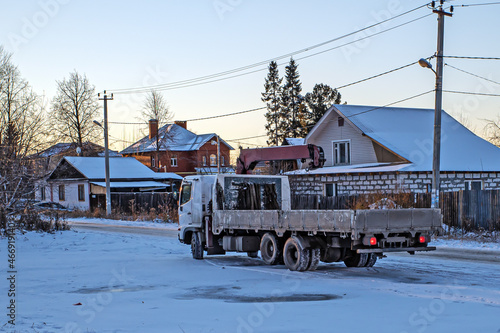 A truck with a manipulator is parked on the side of the road on a winter evening