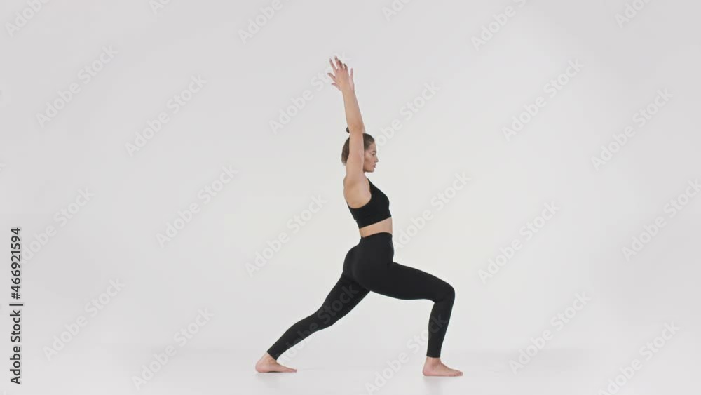 Full length portrait of young active sporty lady practicing Warrior position, doing Virabhadrasana pose, side view Full length portrait of young active sporty lady practicing Warrior position, doing Virabhadrasana pose, side view