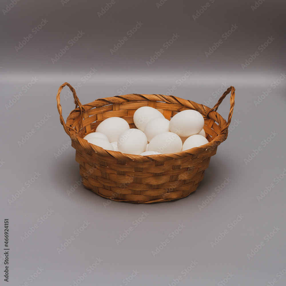 White chicken eggs in a brown wicker basket on a gray background White chicken eggs in a brown wicker basket on a gray background