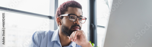 Focused african american businessman in eyeglasses looking at computer monitor in office, banner photo