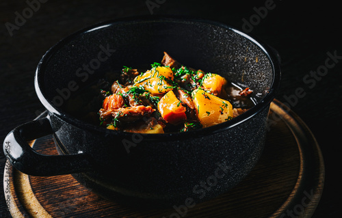 Goulash. Vegetable rague with meat, eggplant, pepper, potato and carrot in black bowl on dark wooden background