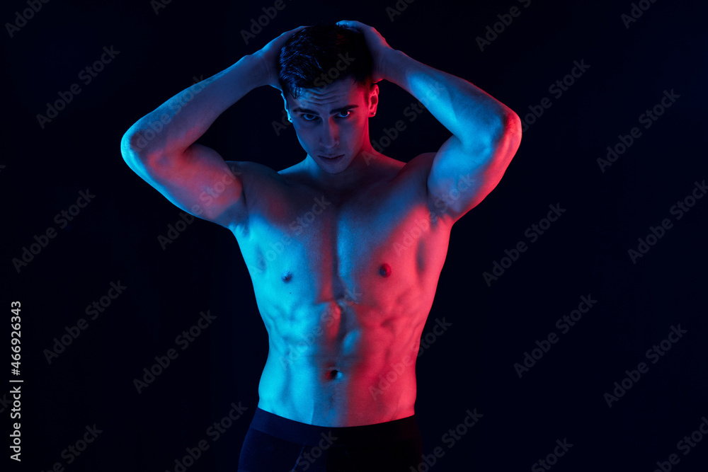 a man with an athletic physique holding his hands behind his head on a black background a man with an athletic physique holding his hands behind his head on a black background