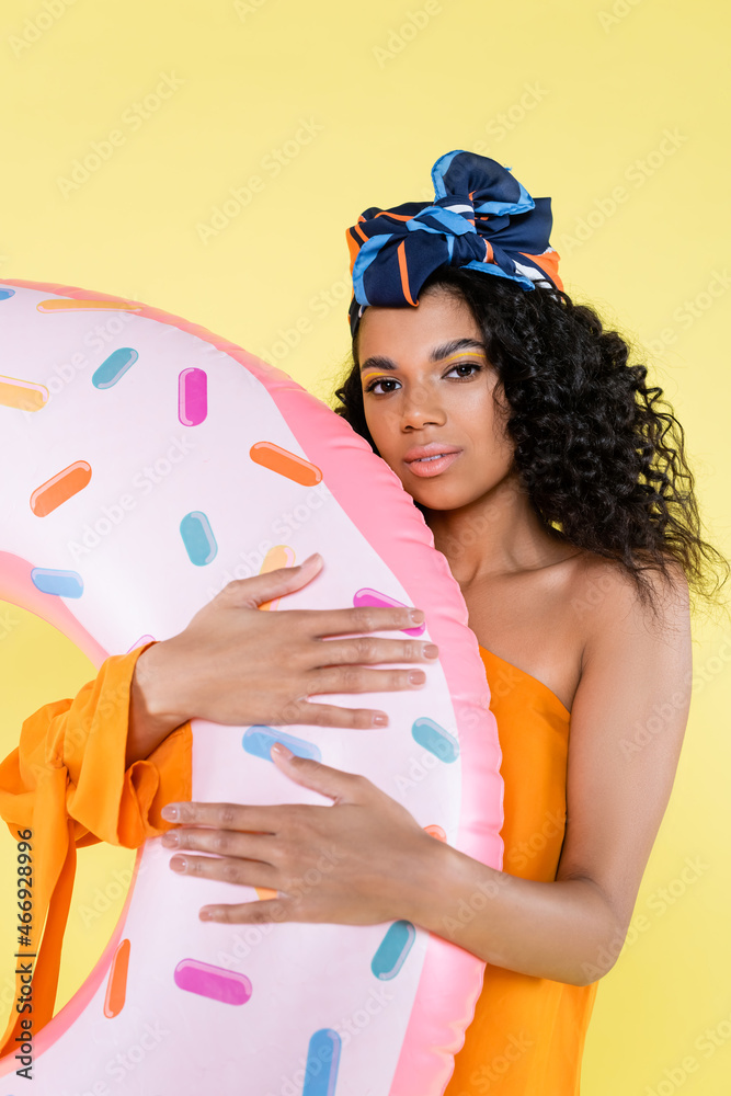 african american woman in headscarf holding inflatable donut isolated on yellow african american woman in headscarf holding inflatable donut isolated on yellow