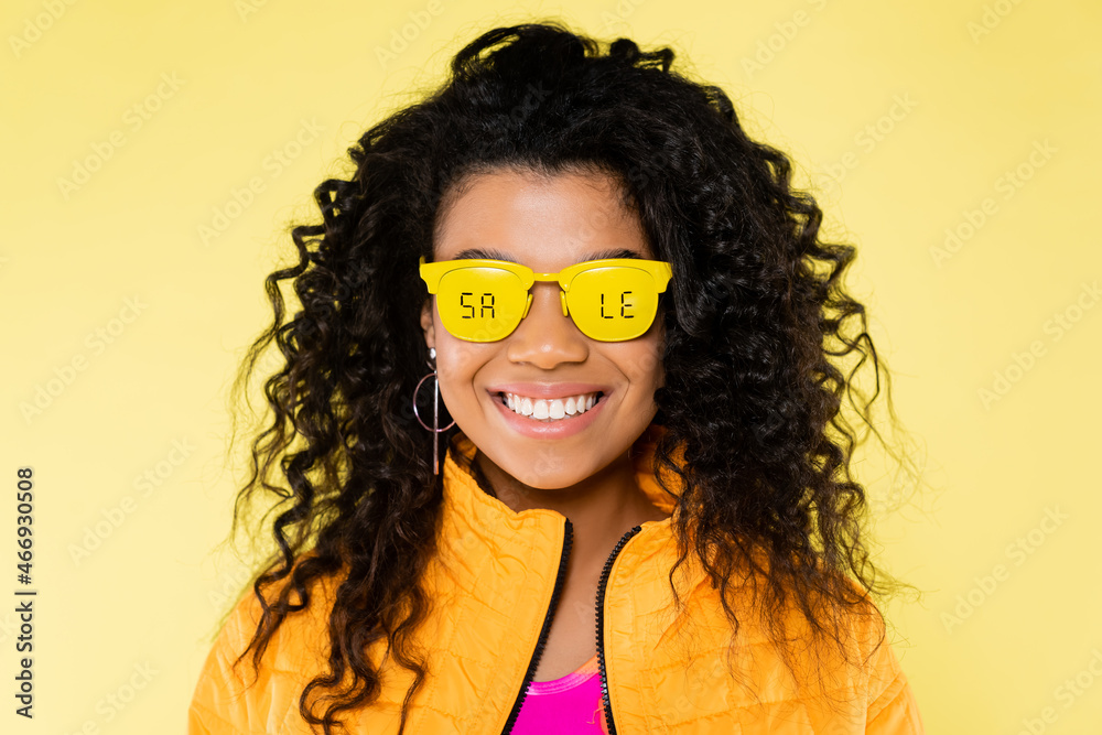smiling african american young woman in sunglasses with sale lettering isolated on yellow smiling african american young woman in sunglasses with sale lettering isolated on yellow