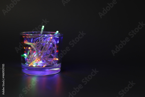 Glass with Christmas lights on black background. © Olesia Prokoshina