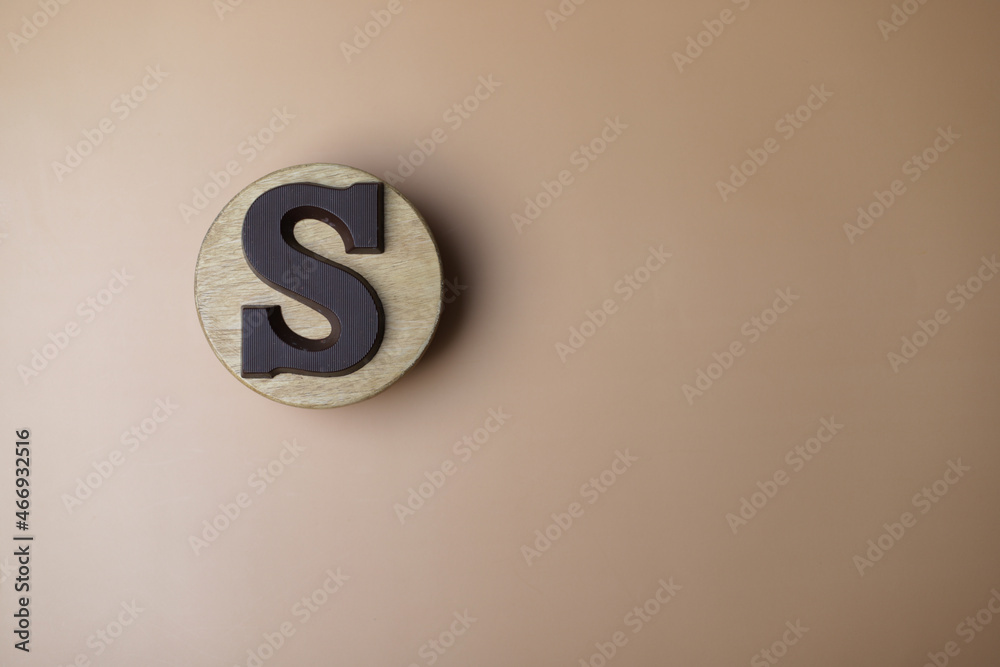 Letter of the alphabet S on the wooden round plate is made from dark milk chocolate on light brown background. Letter of the alphabet S on the wooden round plate is made from dark milk chocolate on light brown background.