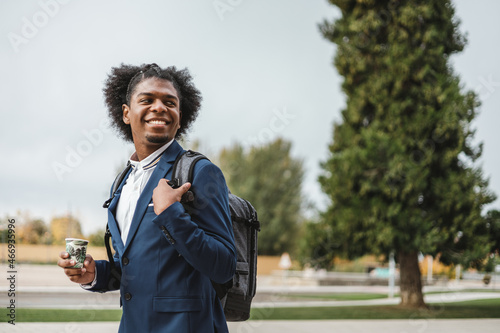 Foto Smiling business afro young man going to work with coffee and backpack