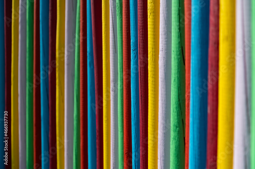 Colorful palisade fence made of wooden poles bars painted with different bright intensive colors. Yellow, green, red, blue and white alternating and forming contrasting pattern. Background lit by sun.