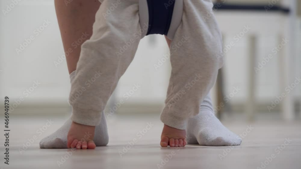 Lovely baby boy learning to walk taking first steps with mother at home, cute child wearing toddler reins walking on the floor with bare foot. High quality 4k footage Lovely baby boy learning to walk taking first steps with mother at home, cute child wearing toddler reins walking on the floor with bare foot. High quality 4k footage