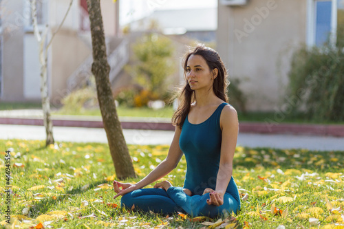 beautiful young girl doing yoga meditation in the autumn park, lotus pose