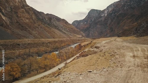 A black SUV jeep car is driving along an empty country road in the huge Katu-Yaryk canyon Chulyshman Valley with a large mountain bubbling river. Altai, Siberia, Russia. People travel along a dirt