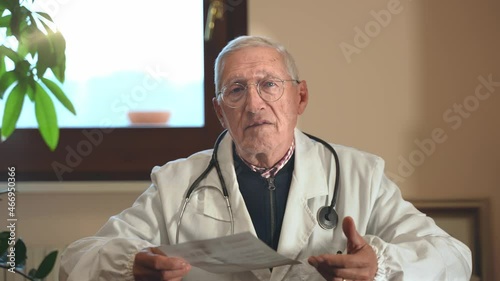 Wallpaper Mural Mature serious doctor with a doctor's jacket and the stethoscope looking directly into camera while having a videocall conference with a patient of a colleague on a computer laptop at the hospital. Torontodigital.ca