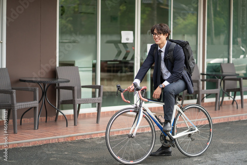Asian businessman in a suit is riding a bicycle on the city streets for his morning commute to work. Eco Transportation Concept.