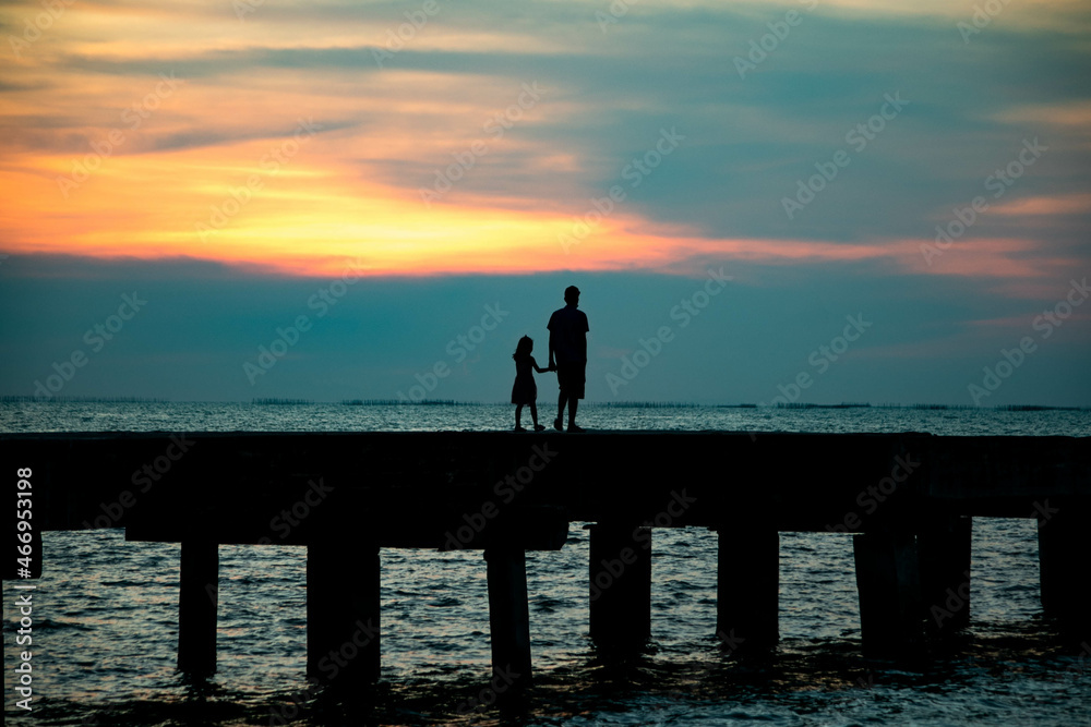 Silhouette of father and daughter walking at sunset on the cement bridge at Chittaphawan Temple, Thailand
