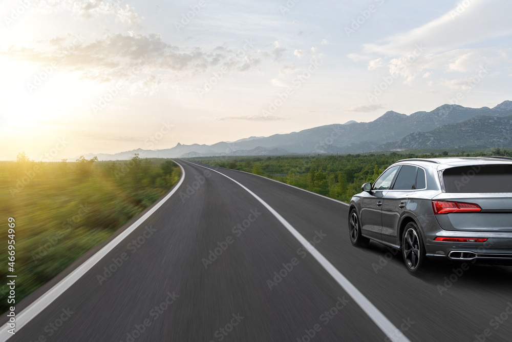 Gray car on a scenic road. Car on the road surrounded by a magnificent natural landscape in the rays of sunset or dawn.