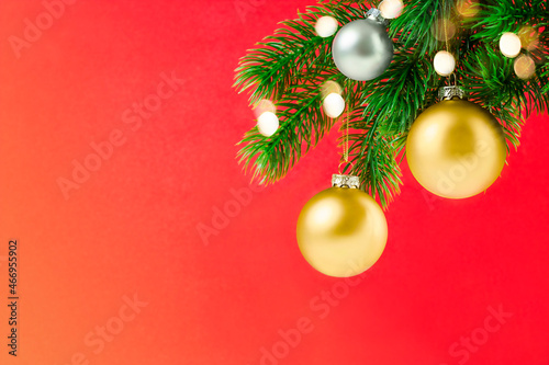 spruce branch with christmas ornaments and defocused lights on red background