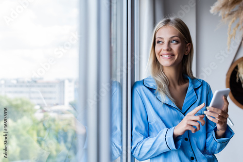 happy young woman holding cellphone and looking at window