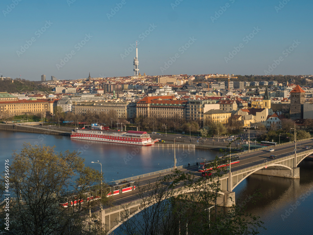 Scenic aerial view of Prague Old and New Town architecture roof top and Manes Bridge over Vltava river with houseboat and tram seen from Letna hill park, spring sunny day, blue sky, Czech Republic